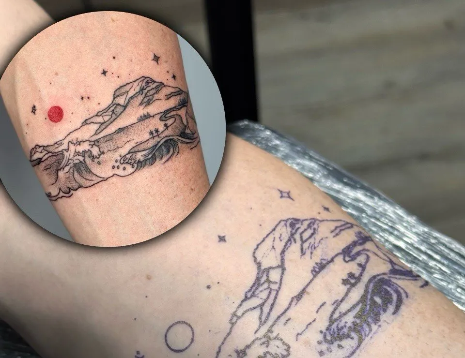 Stencils uz rokas un ieliktnī gatavais tetovējums ar kalniem, viļņiem un sarkanu sauli